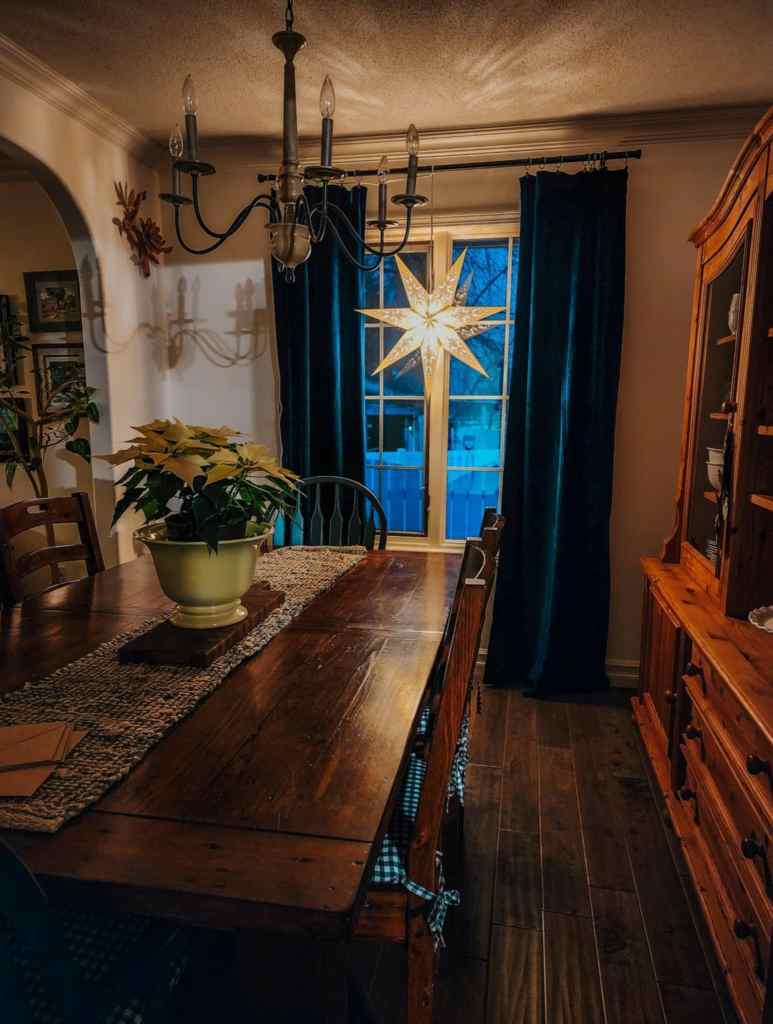 A Christmassy dining room with star in the window and blue velvet curtains. 