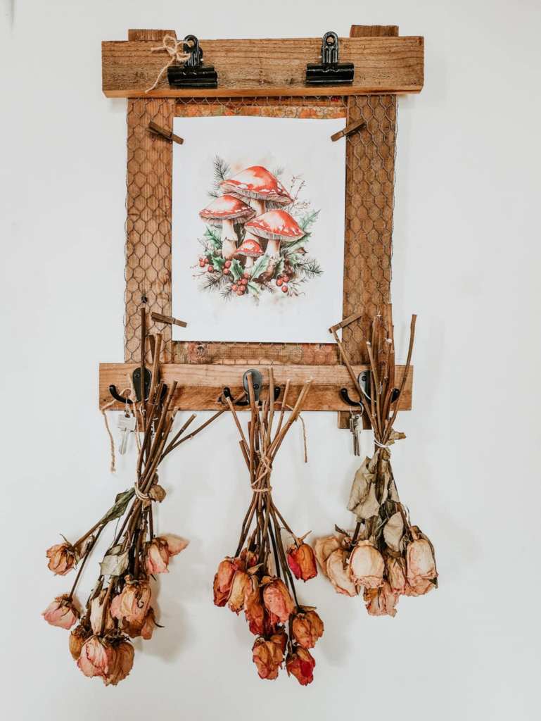 A rustic keyholder with a picture of mushrooms pinned to the chicken wire, and dried roses hanging from the key hooks. 