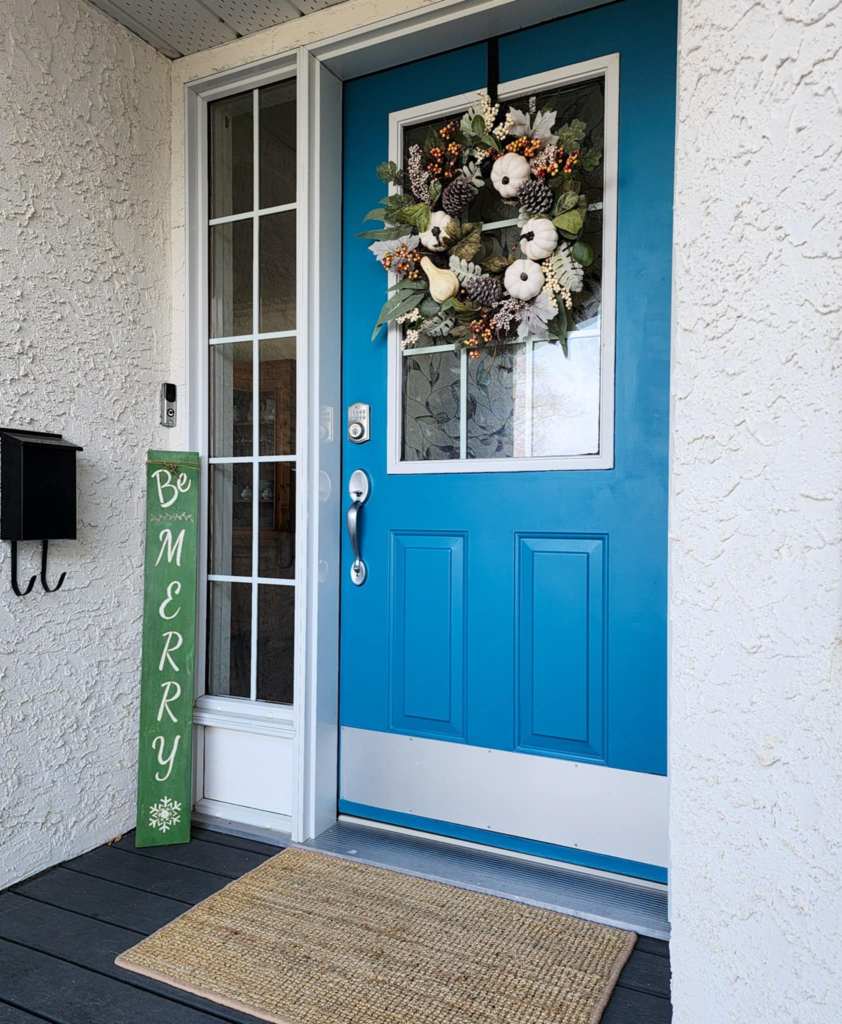A holiday porch sign and a blue door. 