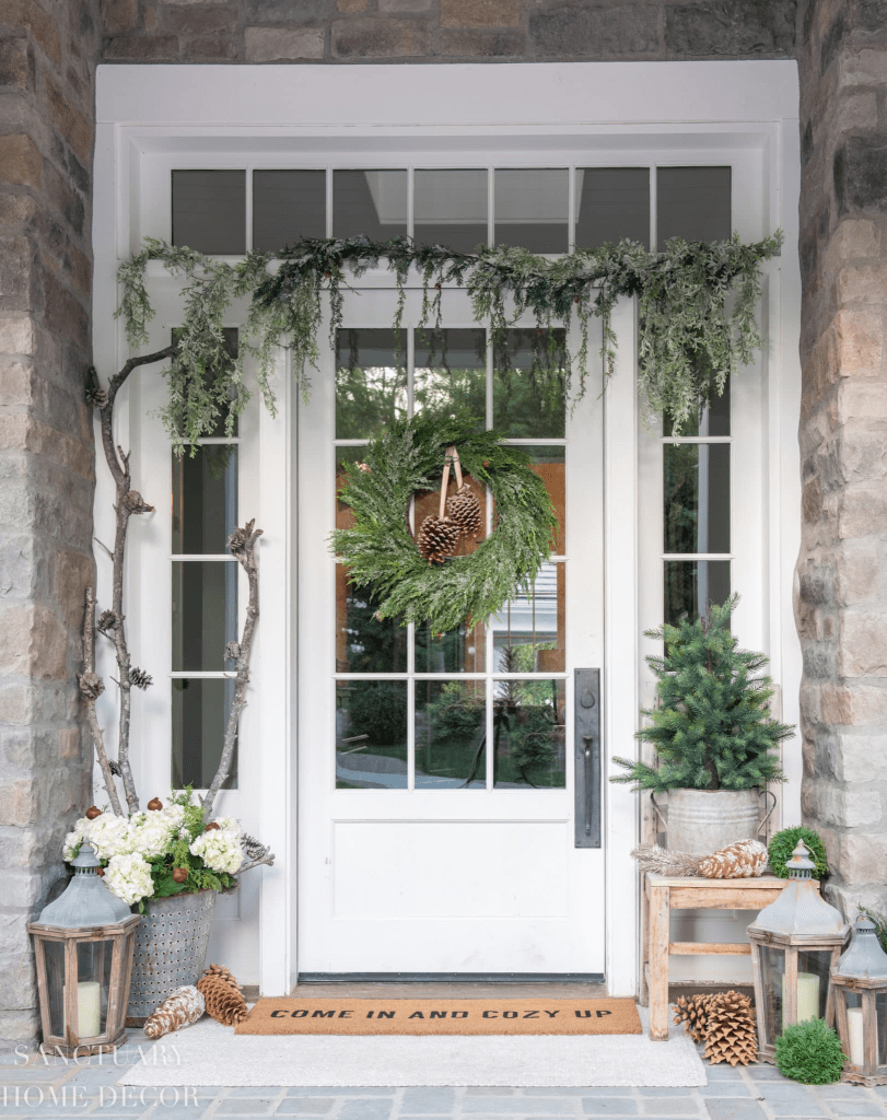 A Christmassy dressed front porch. with wreath on the door, lanterns and   planters beside the doorway.  