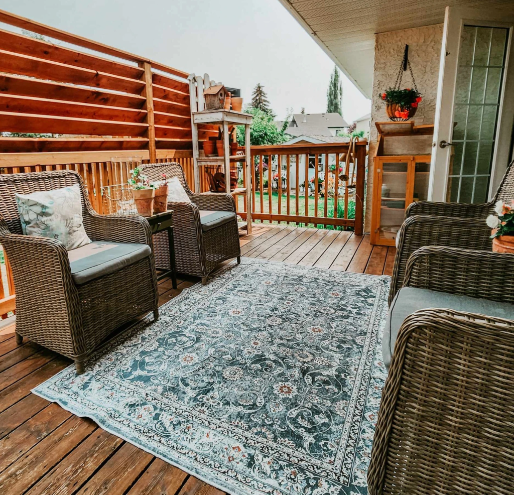 An outdoor deck with 4 wicker chairs and a blue patterned maching washable rug. 
