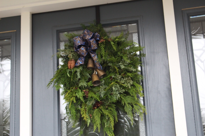 A fluffy evergreen wreath with cowbells and a big blue and gold bow. 