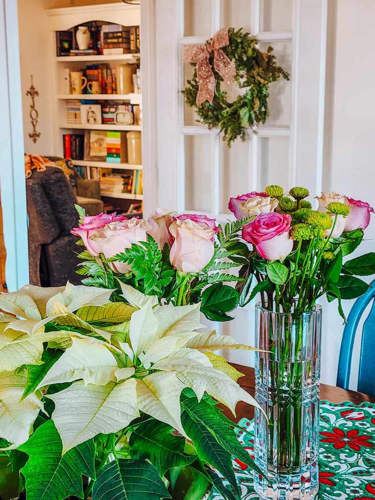 A white poinsettia and two bouquets of pink roses with green little mums. A wreath with a pink bow in the background to tie it all together. 