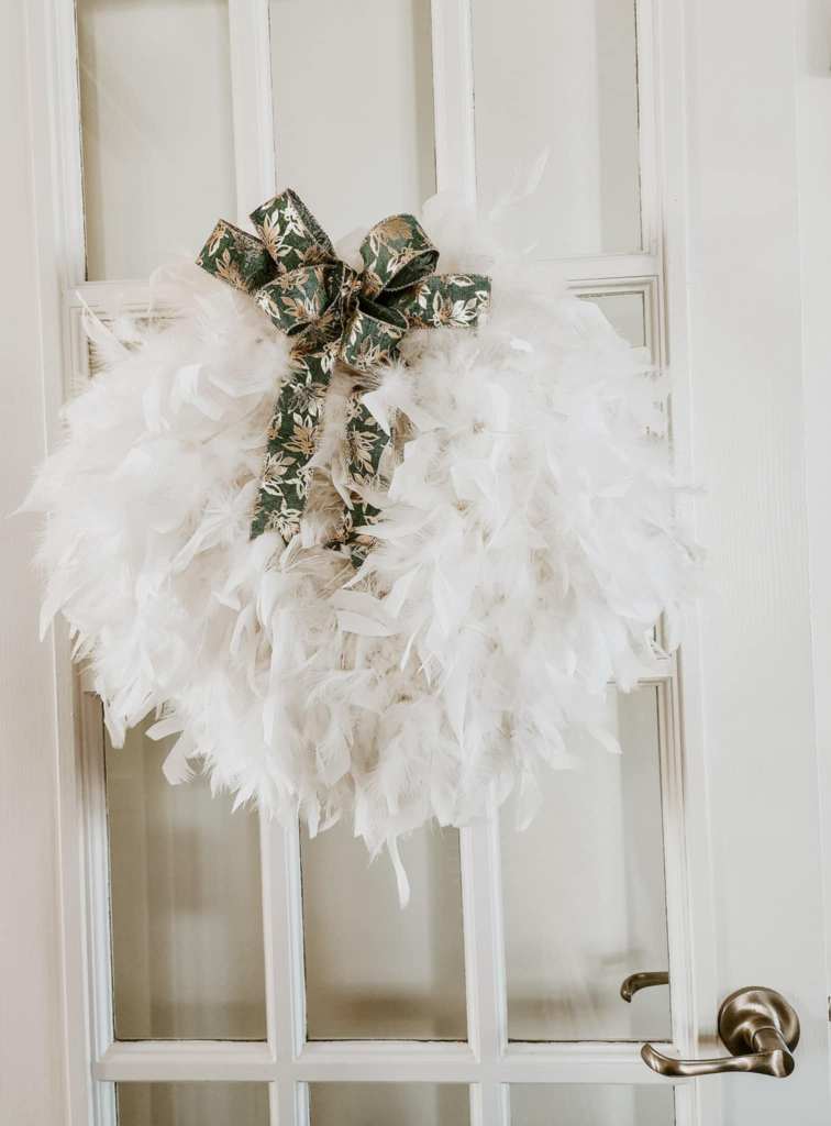 A white fluffy wreath made from boas, with a green and gold bow on it. 