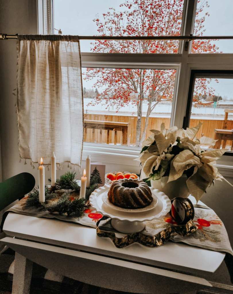 A Christmas table set with a gingerbread cake, poinsettia, advent candles, and mandarin orange.