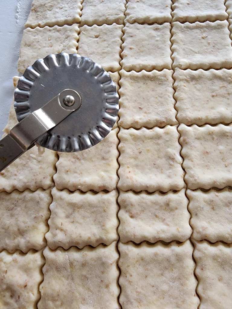 Homemade sourdough crackers being cut with a pastry cutter.