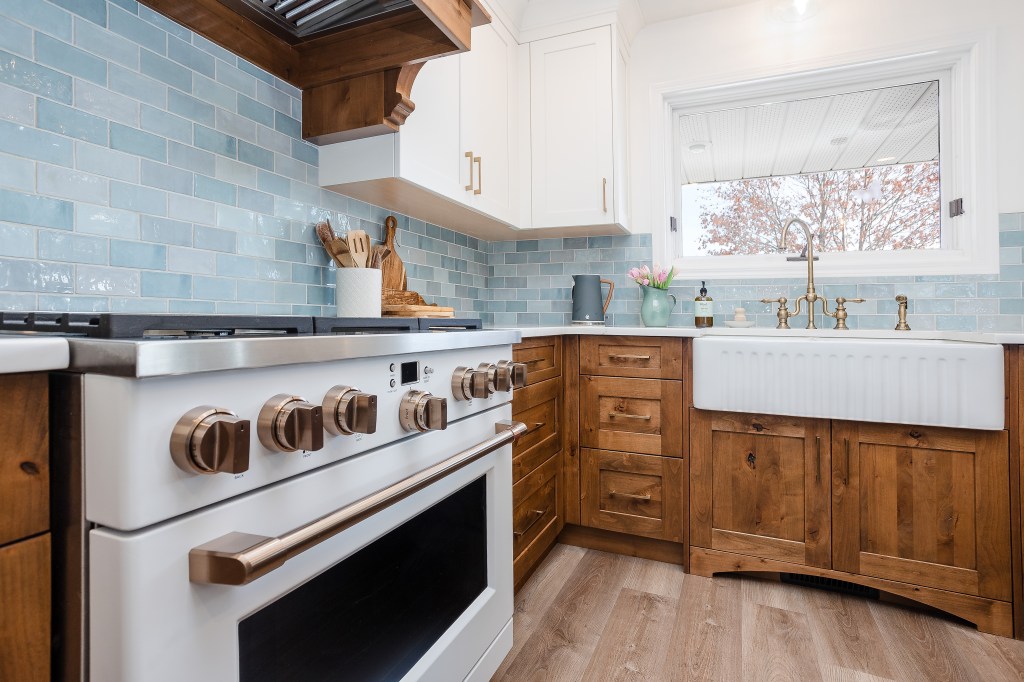 A wood and white kitchen with a ribbed farmhouse sink and brass faucet. 