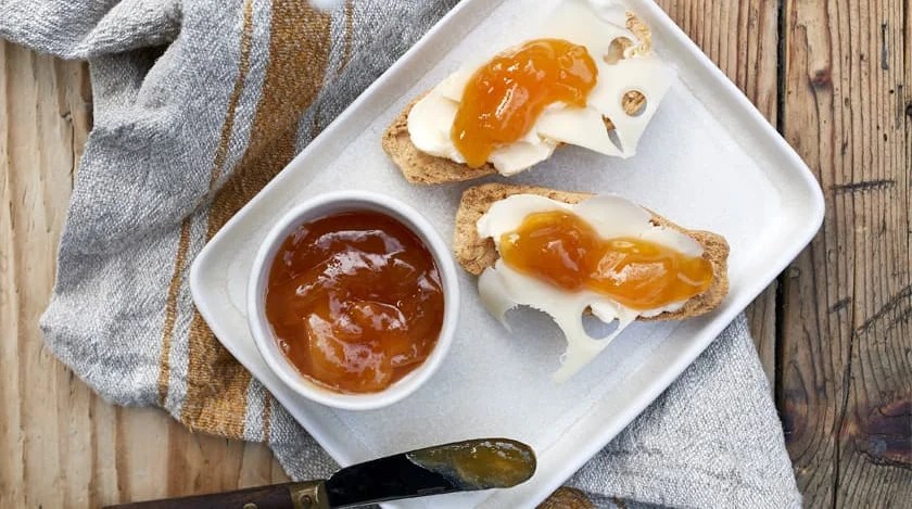 A bowl of marmalade, two rusks with cheese and jam on them. 