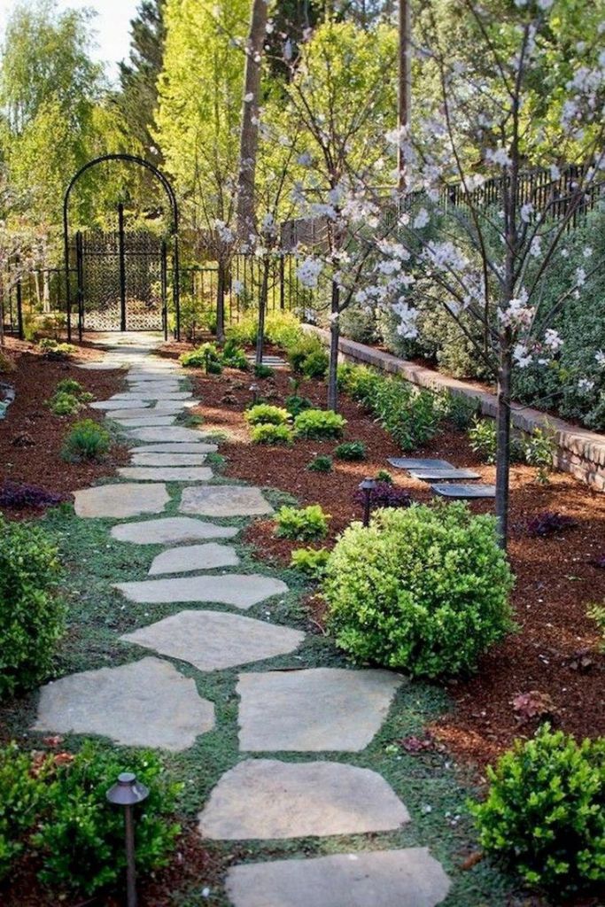 a pathway in mulch with creeping thyme, apple trees in bloom, and small plantings. 