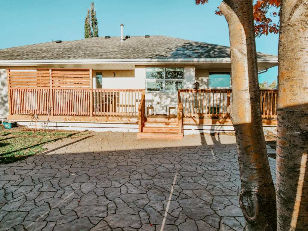 Treated wood railings and stairs along a large deck at the back of a house. A patio made of irregular shaped interlock patio stones. 