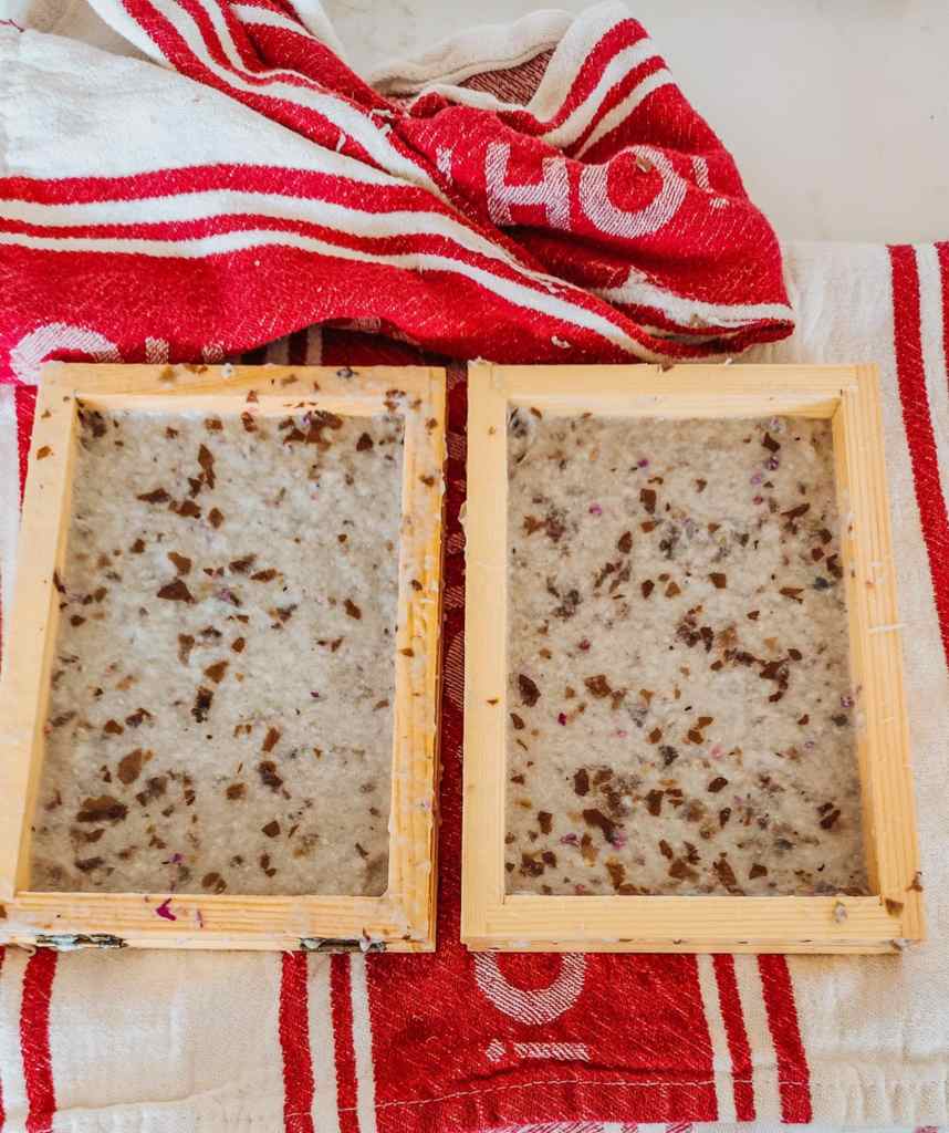 Two wooden paper-making molds filled with wet, textured paper pulp, sitting on a red and white striped towel.