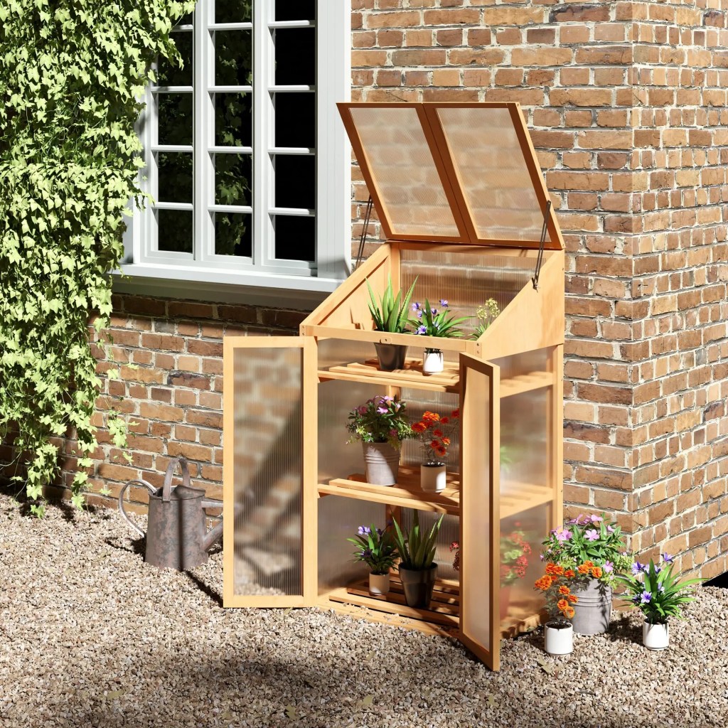 A wooden greenhouse cabinet with plants and flowers, positioned against a brick wall, featuring open doors and a clear top lid.