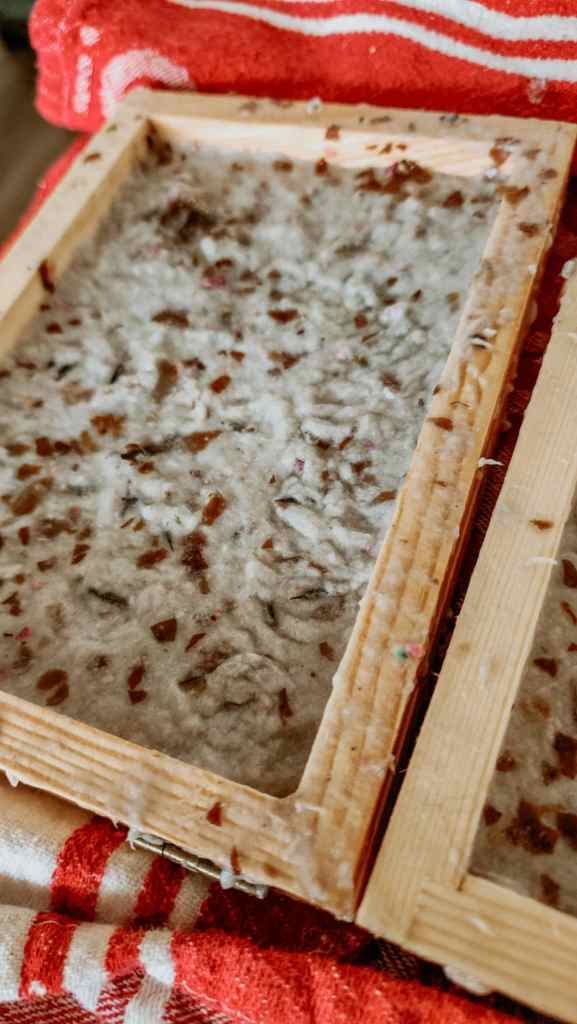 Close-up of handmade paper pulp in a rectangular mold, resting on a striped red and white towel.