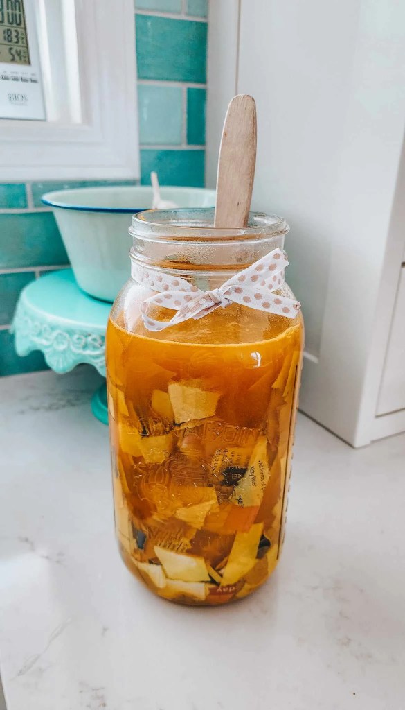 A mason jar filled with torn pieces of paper soaking in turmeric solution, topped with a wooden stick and tied with a polka dot ribbon.