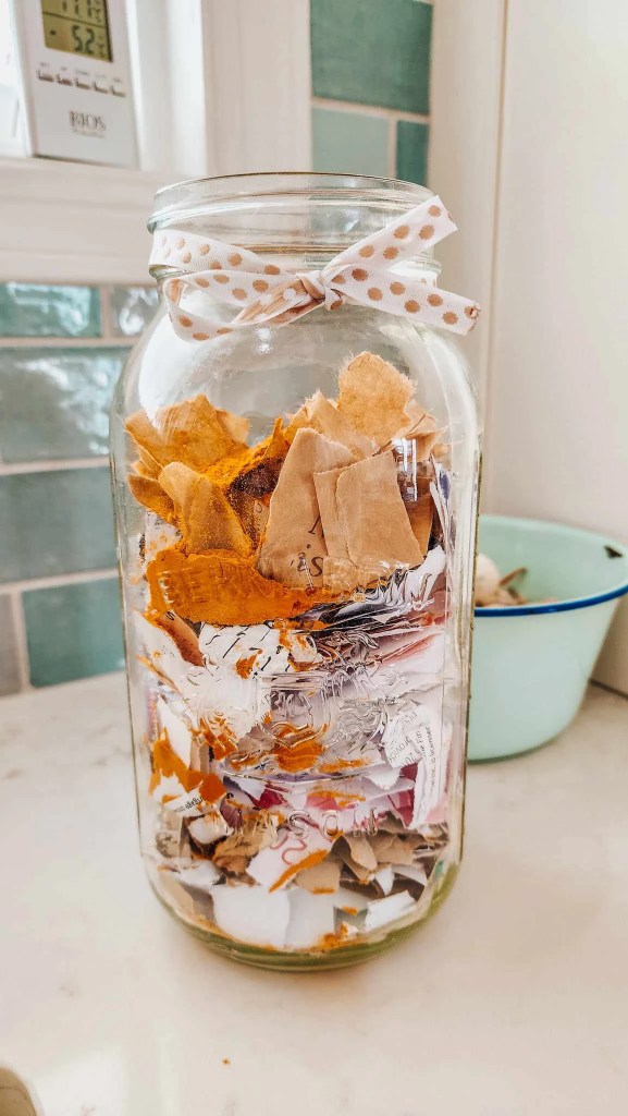A glass jar filled with colorful scraps of paper and turmeric powder, adorned with a polka dot ribbon on top.