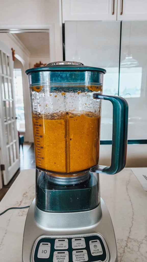 A blender filled with a golden yellow mixture on a countertop, with a glimpse of a kitchen in the background.