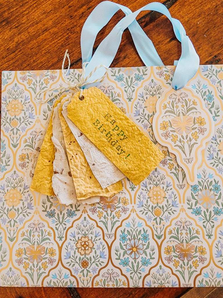 A collection of handmade seeded gift tags in various shades of yellow and cream, displayed on a decorative gift bag with floral patterns and light blue ribbons.