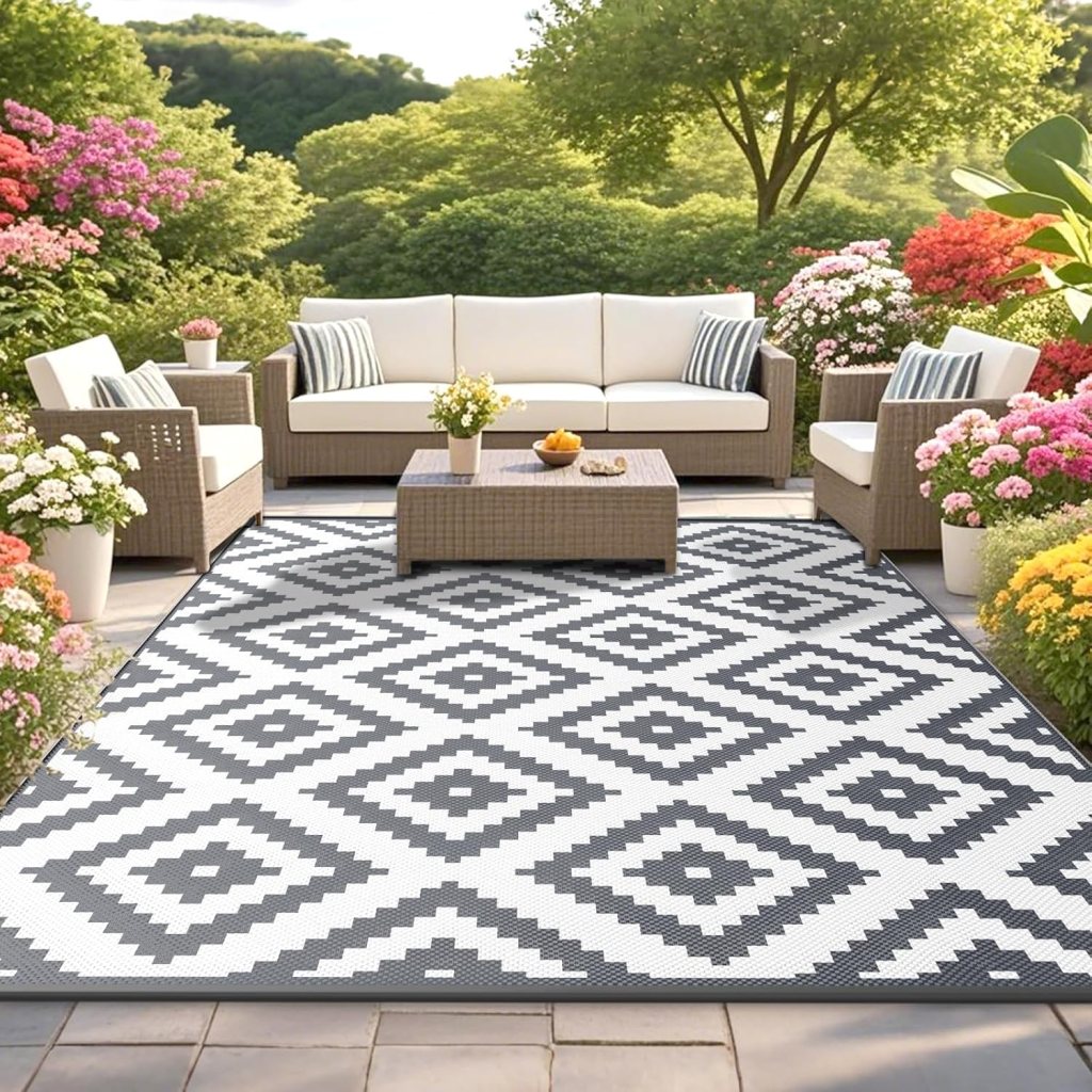 An outdoor seating area featuring a modern rug with a diamond pattern in black and white, surrounded by colorful flowers and greenery.