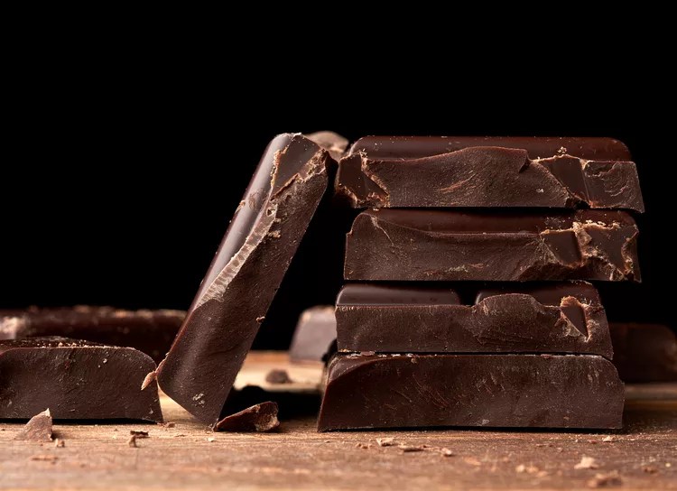Squares of dark chocolate stacked on a wooden surface. 
