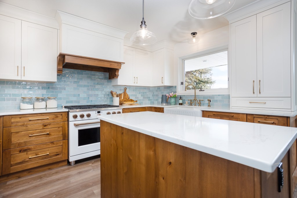 A modern kitchen featuring white cabinets, a wooden island, a gas stove, and a light blue tile backsplash, with natural light streaming through a window.