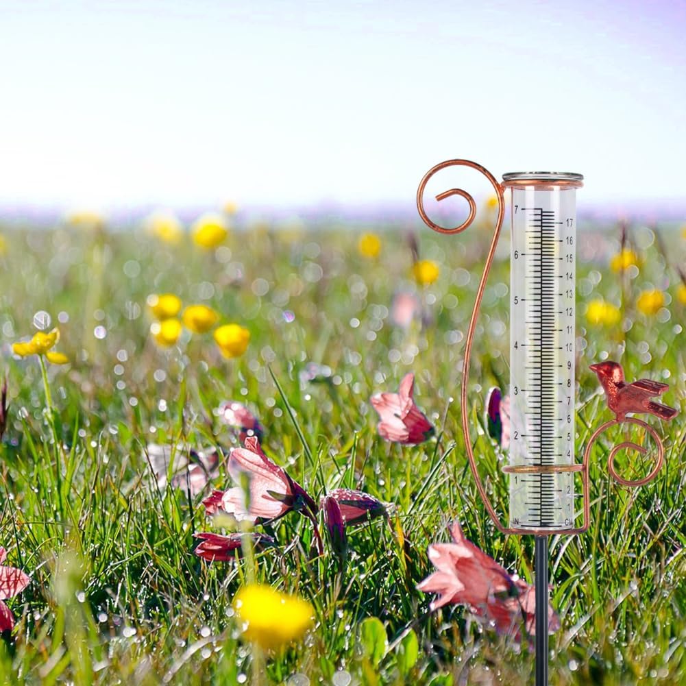 A decorative rain gauge in a field of flowers, featuring a copper design with birds and measuring markings.