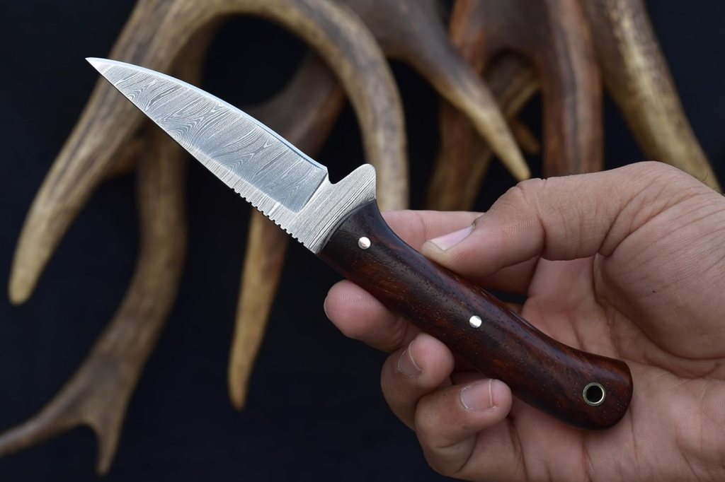 A person holding a small knife with a wooden handle and decorative blade, set against a backdrop of antlers.