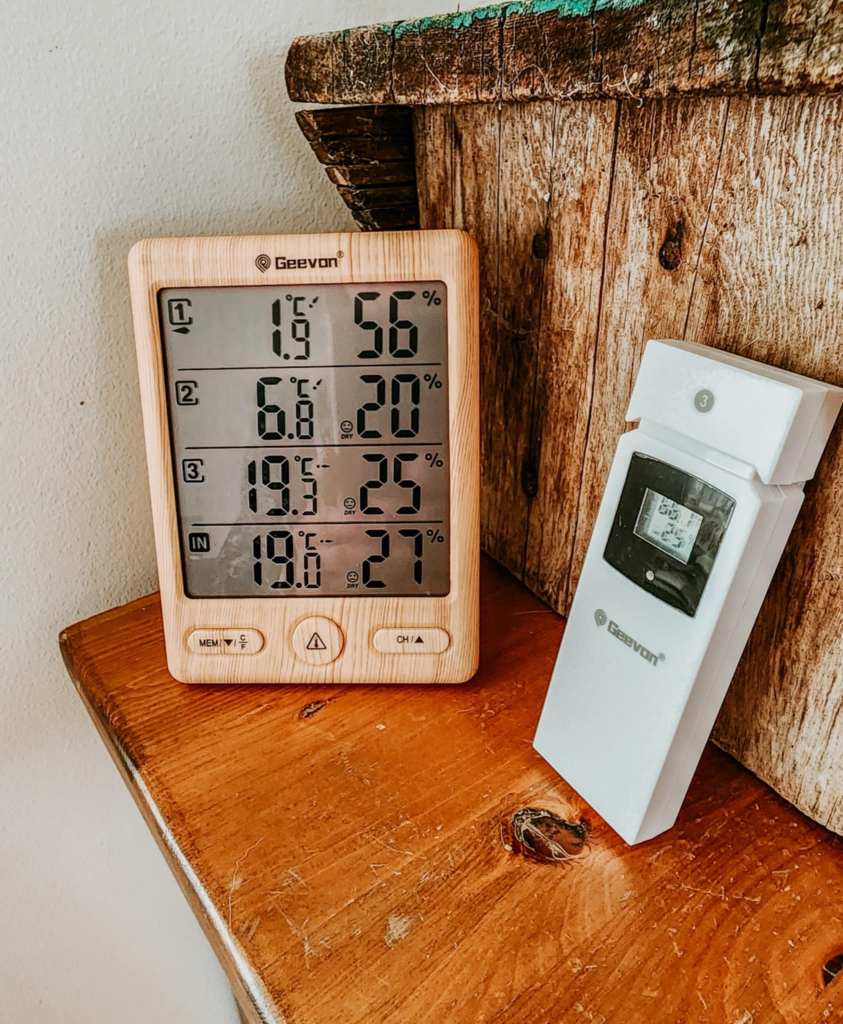 Digital thermometer and hygrometer displaying indoor and outdoor temperature and humidity on a wooden table.
