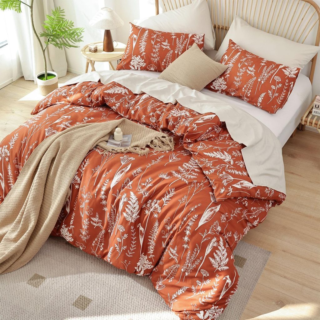 A cozy bed with an orange floral duvet cover, matching pillows, and a neutral throw blanket, set in a bright and airy bedroom.