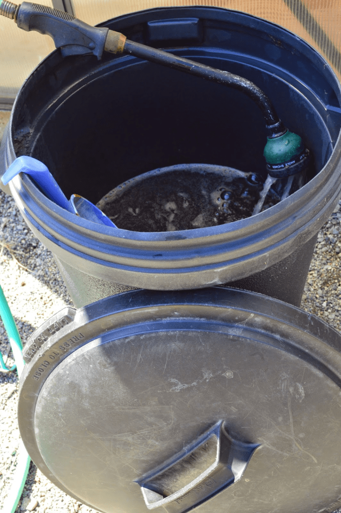 A black bucket filled with dark liquid, with a hose attached, likely for making manure or compost tea for organic gardening.
