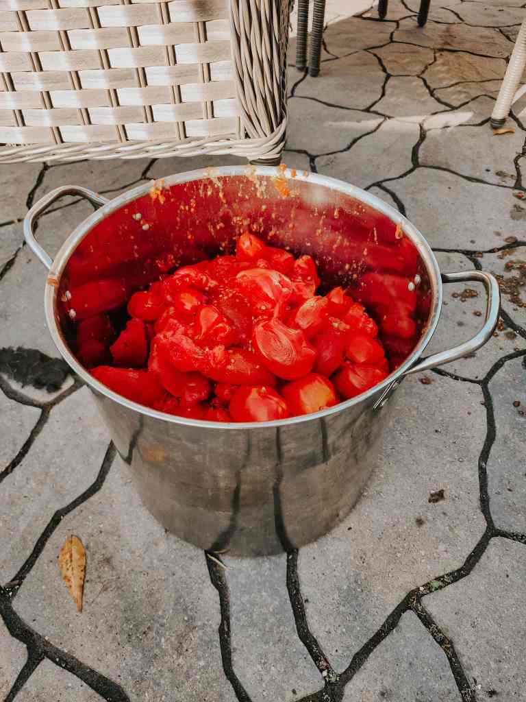 A large pot filled with chopped red tomatoes, sitting on a stone patio, with a wicker chair visible in the background.