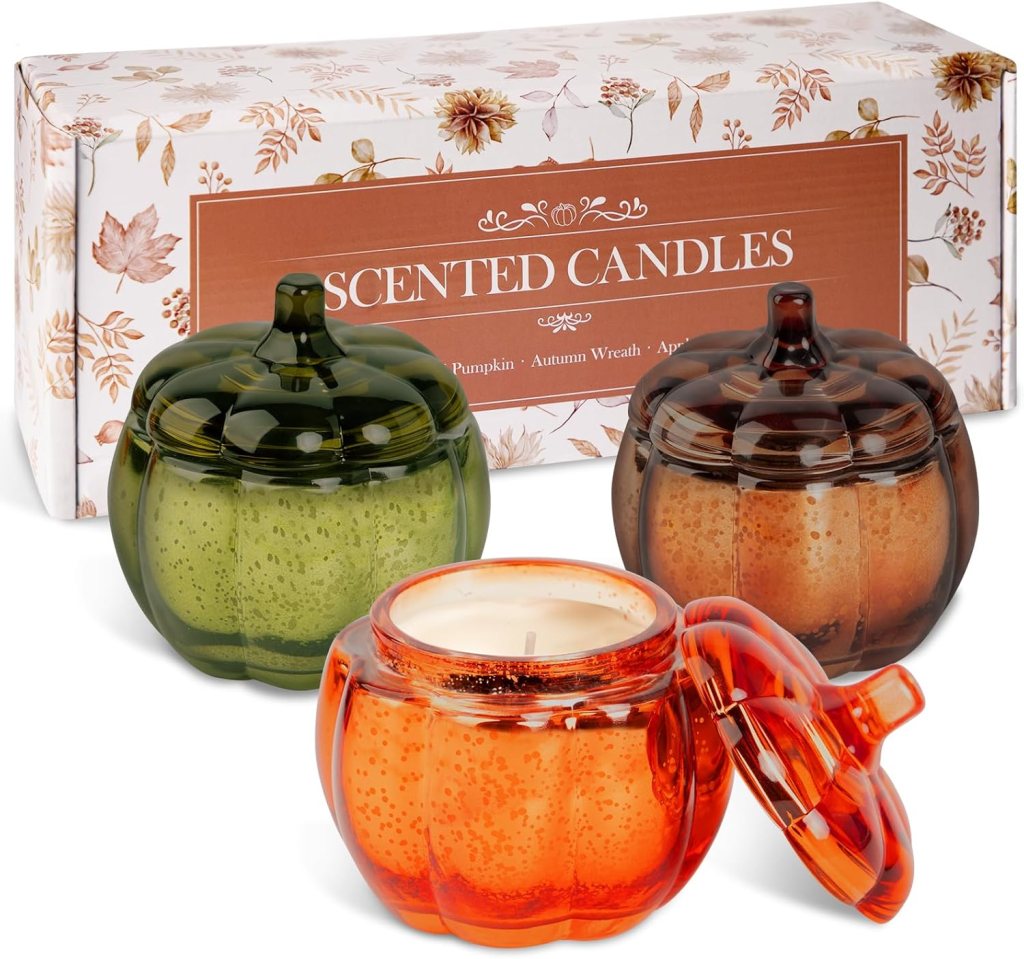 A set of three scented candles shaped like pumpkins in green, orange, and brown, displayed in a decorative box with autumn-themed designs.