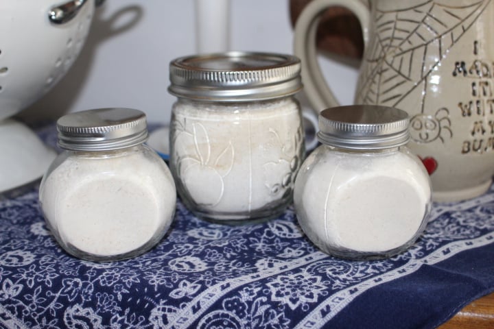 Three glass jars filled with homemade spice powders, including garlic powder and chili powder, arranged on a blue patterned tablecloth.