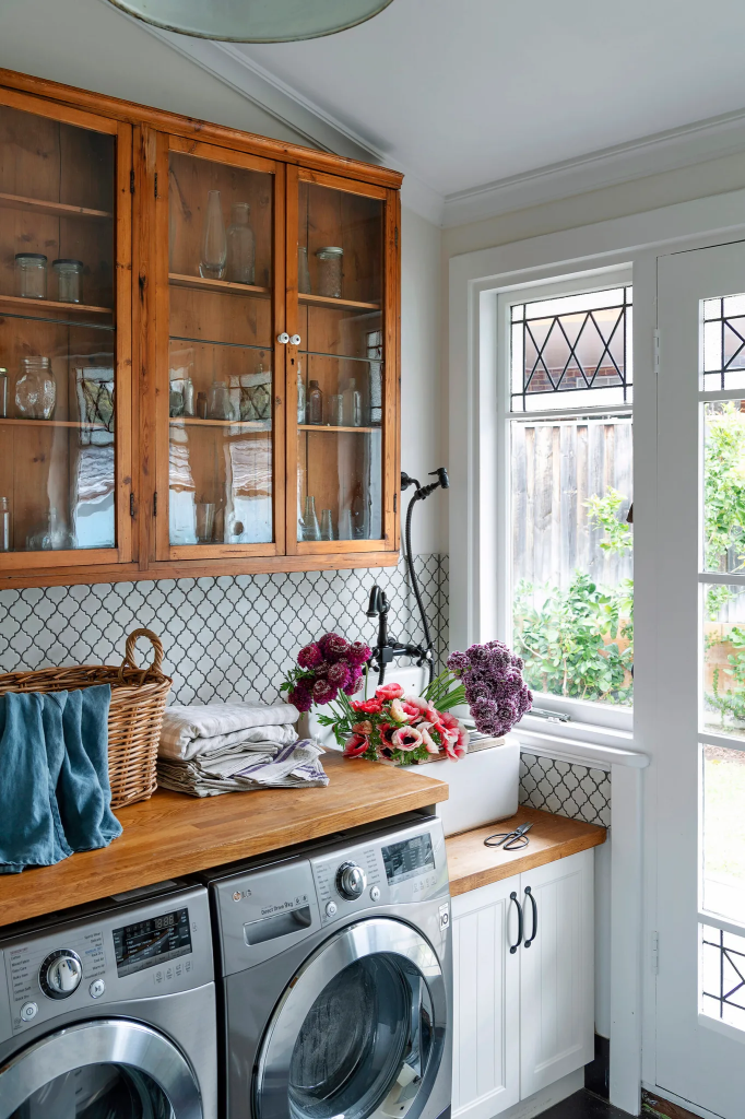 A cozy laundry room featuring modern appliances, a wooden countertop, a basket of clean laundry, and fresh flowers near a window.
