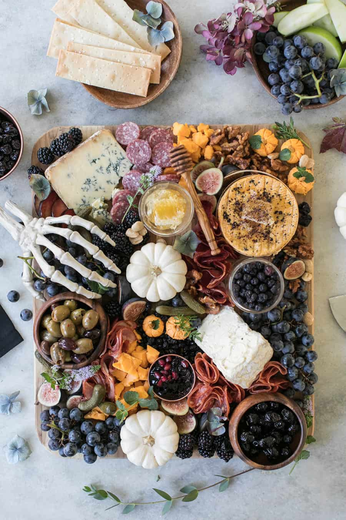 A beautifully arranged Halloween charcuterie board featuring a variety of cheeses, meats, fruits, and decorative pumpkins set on a light surface.