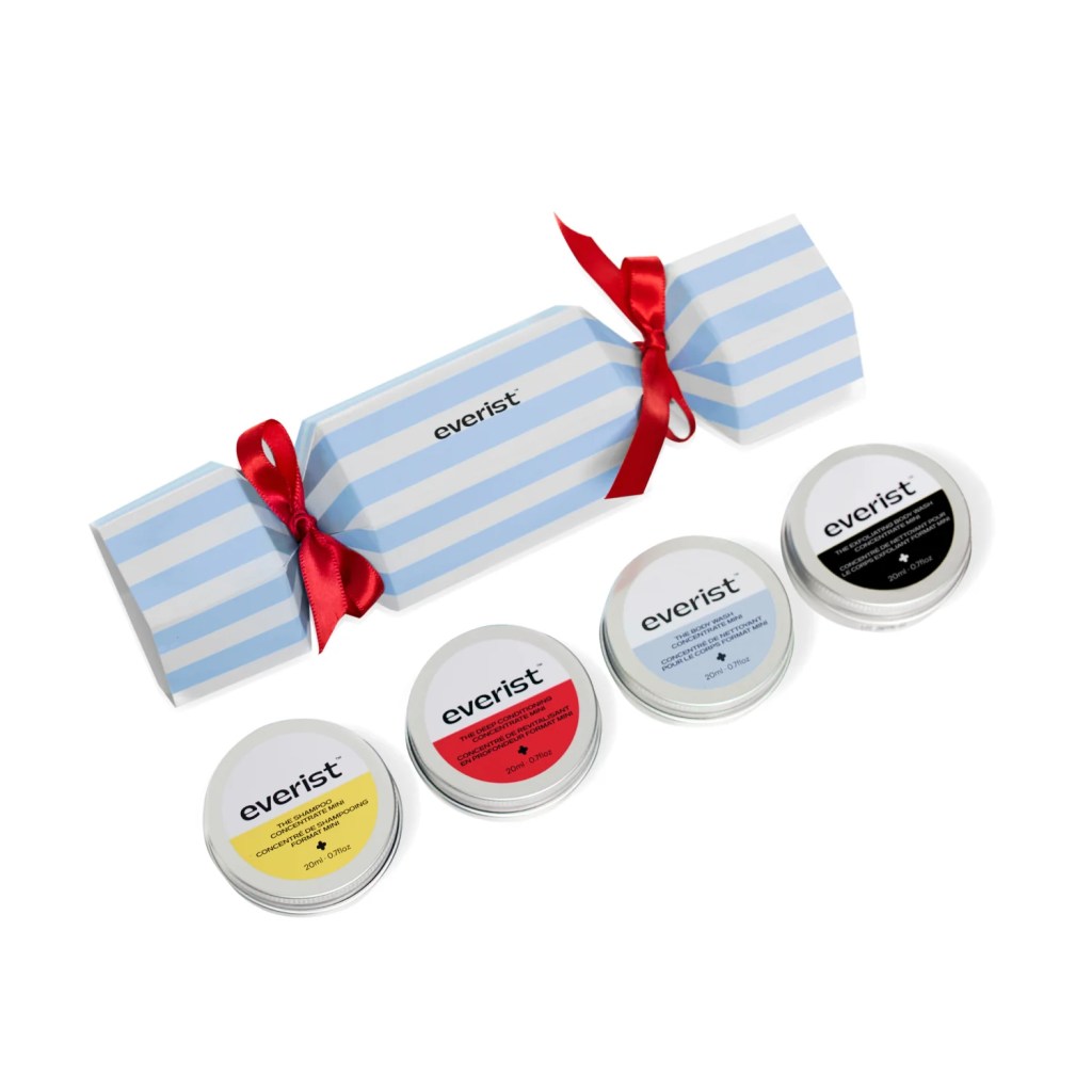 A holiday gift set featuring a striped blue cracker with a red ribbon, accompanied by four small tins of skincare products from Everist, each labeled with different colors.