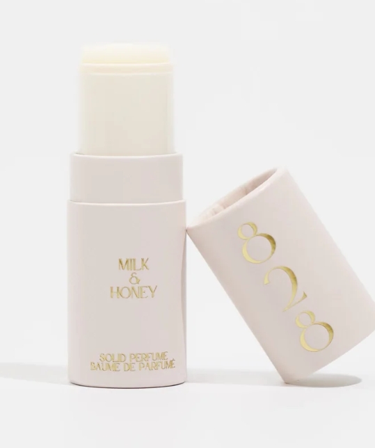 A close-up of a solid perfume stick labeled 'Milk & Honey,' showcased in a minimalistic, pale pink container with gold-colored text.
