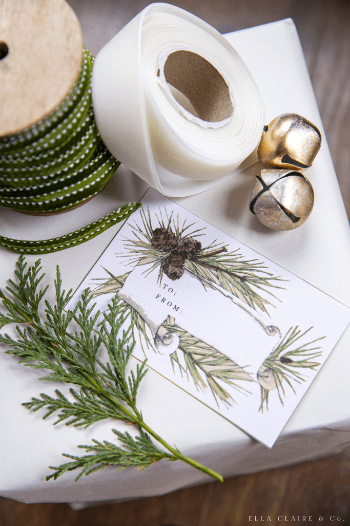 A collection of gift-wrapping supplies, including green polka-dotted ribbon, white tape, golden bells, and a decorative gift tag featuring pine branches and pinecones.