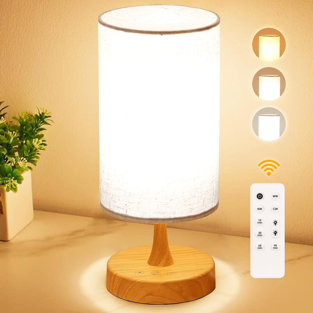 A modern table lamp with a cylindrical shade emitting soft light, positioned on a wooden base. A remote control is displayed next to the lamp.