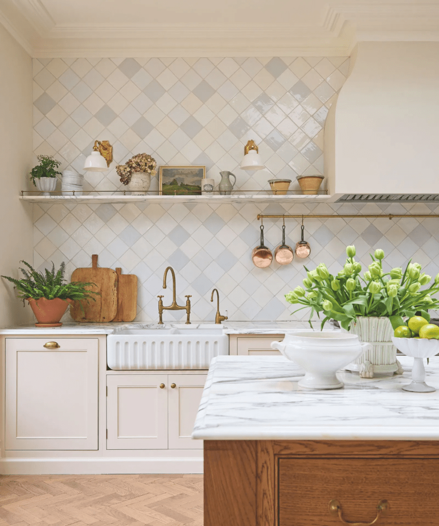 A beautifully designed kitchen featuring white cabinetry, a large farmhouse sink, and marble countertops, complemented by a wood accent island and decorative elements like potted plants and copper cookware.