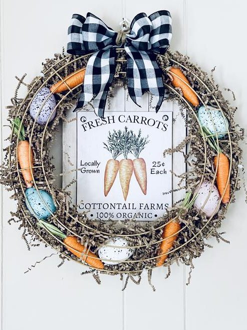 A decorative wreath featuring fresh carrots and painted eggs, with a central sign displaying 'Fresh Carrots', 'Locally Grown', and pricing details. The wreath is adorned with a black and white checkered bow.