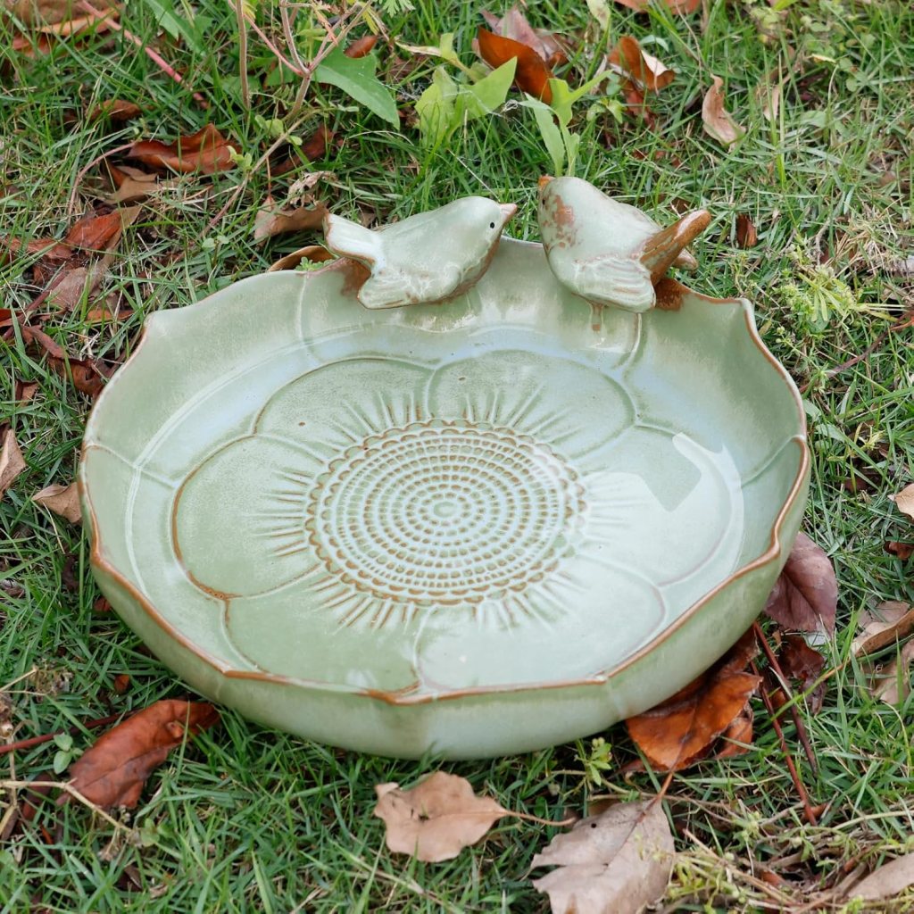 A ceramic birdbath bowl with two small birds on the edge. 