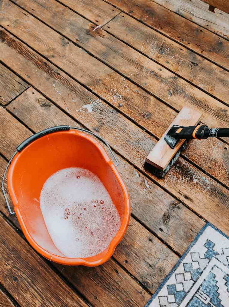 Cleaning a deck with a bucket of soapy water and a deck brush. 