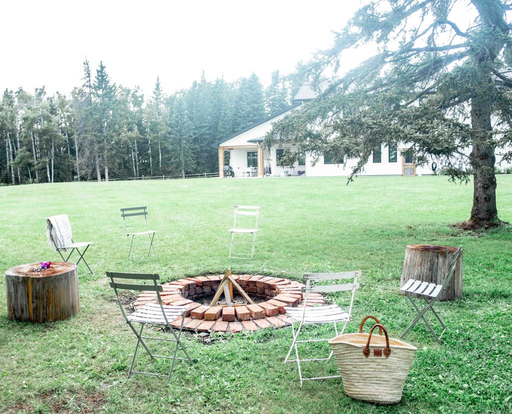 A brick firepit in a yard of green grass, with foldable chairs around it. 
