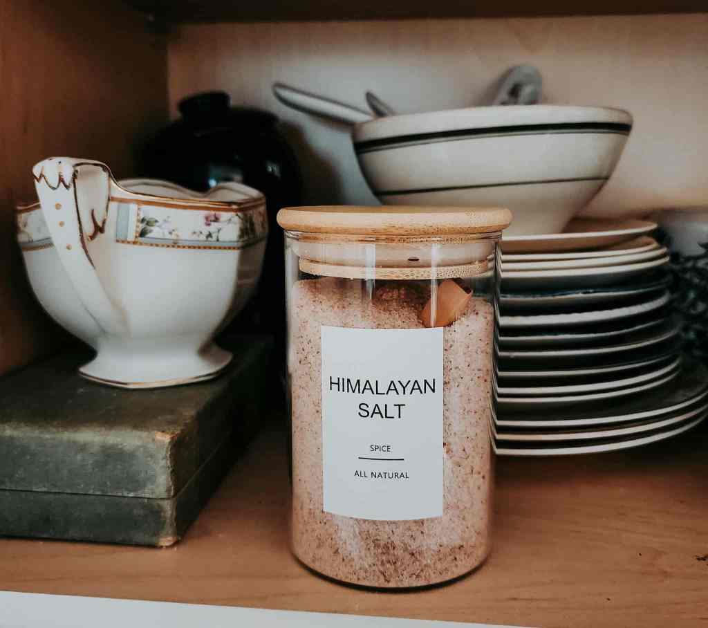 A jar of Himalayan salt inside a cupboard with a gravy boat, stacks of plates, and an antique bowl with green trim.