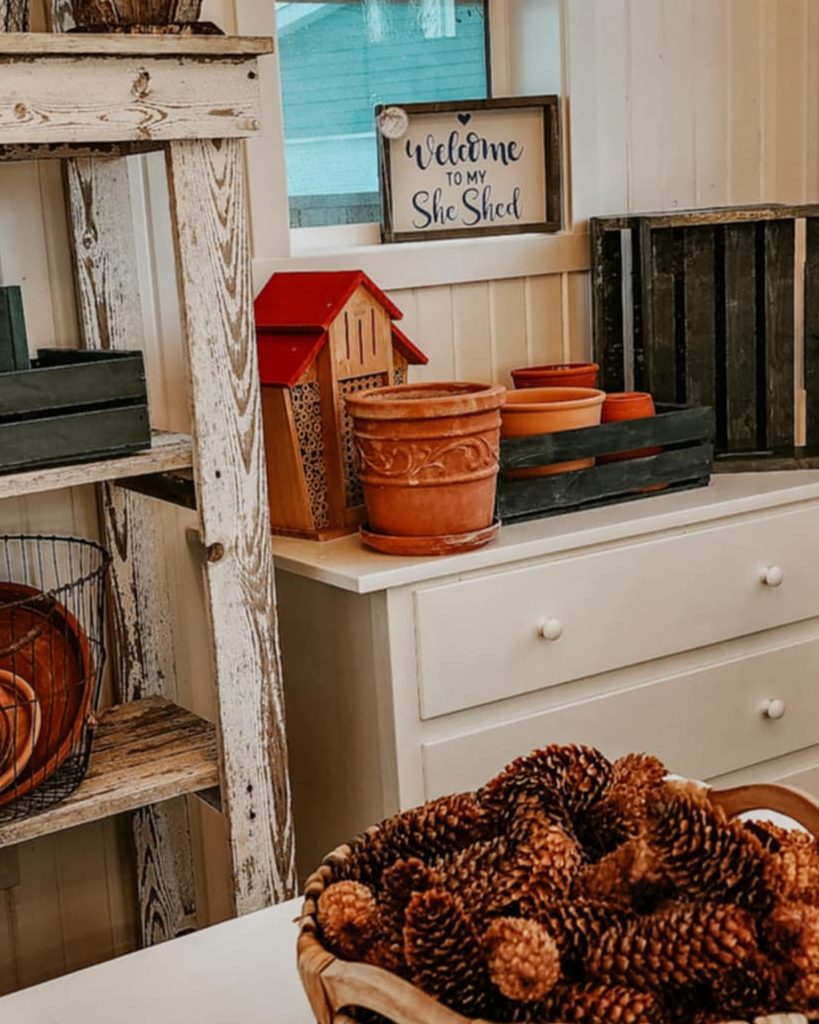 A dresser in a potting shed with a bee house, clay pots, and blue crates.