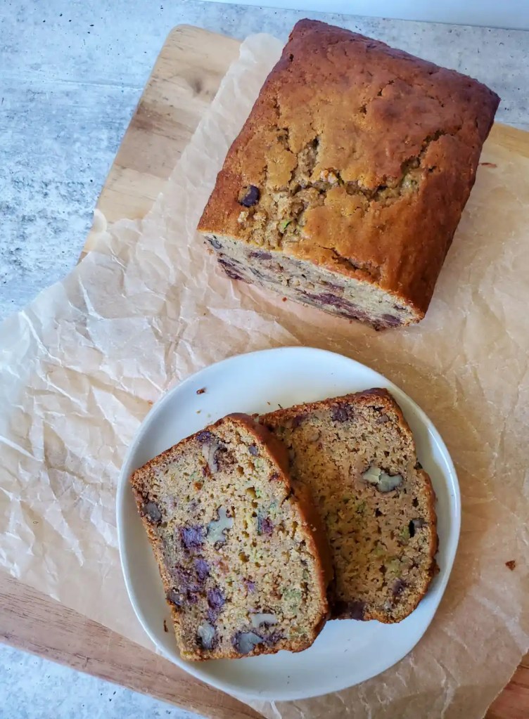 Two slices of zucchini bread with walnuts on a white plate and sitting on parchment paper.